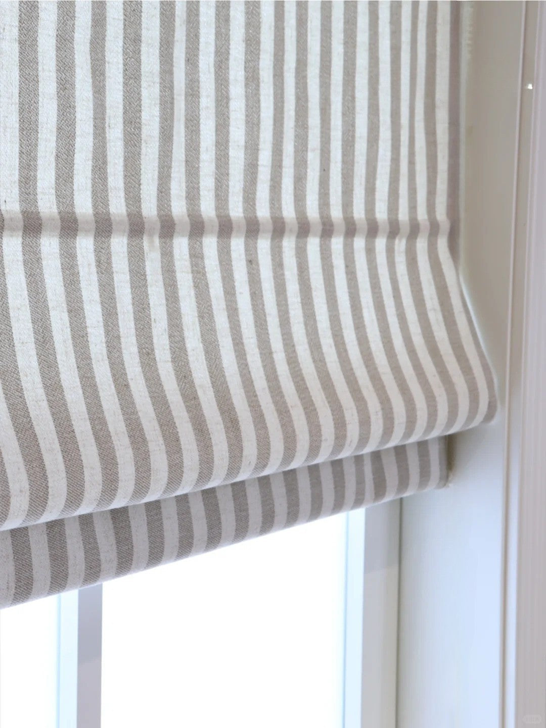 Close-up of beige and white striped Roman shades with cordless lift system covering a window