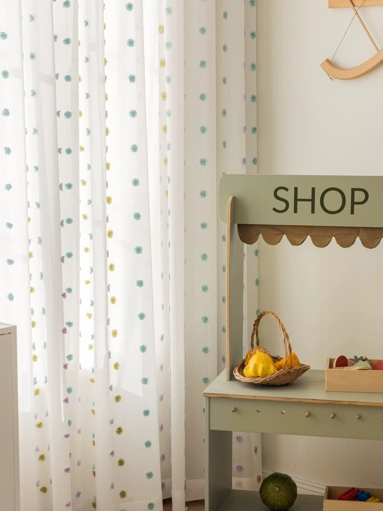 Colorful candy sheer curtains with playful pom-poms for kids' rooms.