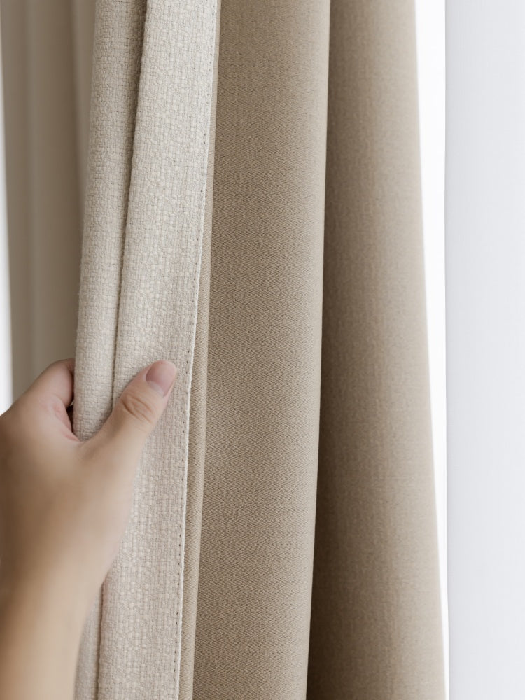 Hand holding heavyweight linen blend blackout curtain in beige tone.