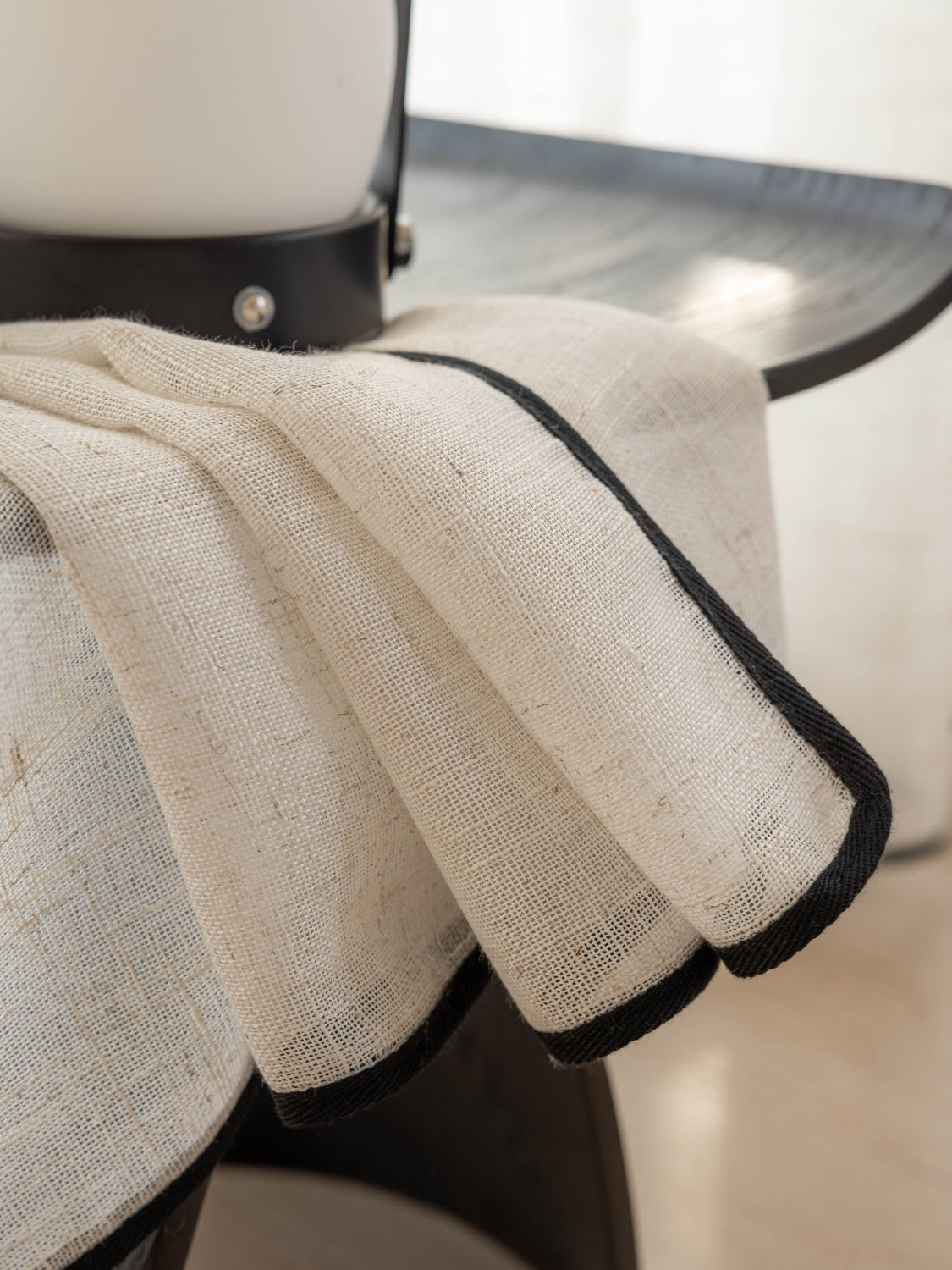 Sheer linen curtains with black trim showcased on a modern chair.