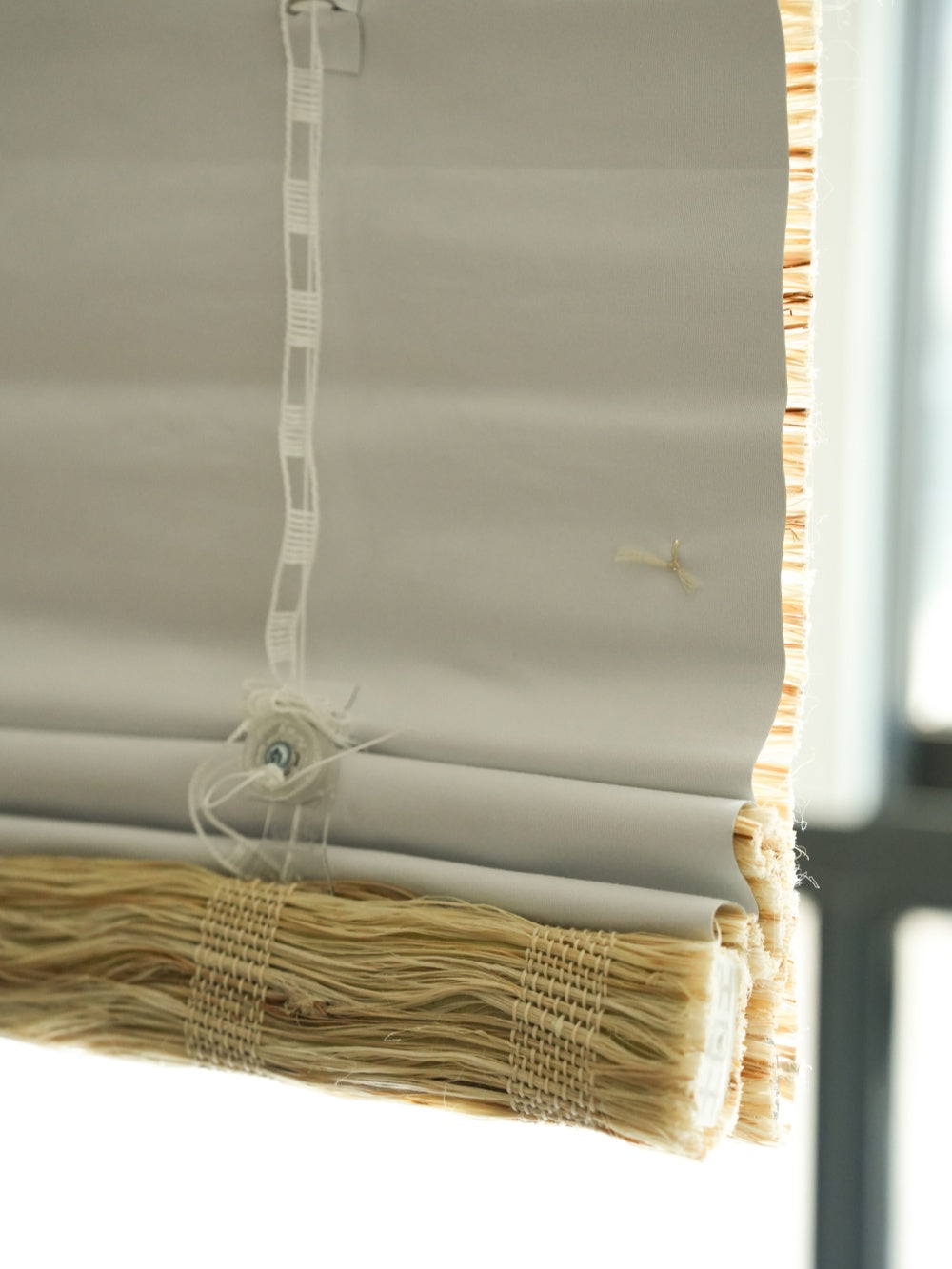 close-up of honey-colored woven shades made from natural ramie fiber with textured edges and light filtering through a window