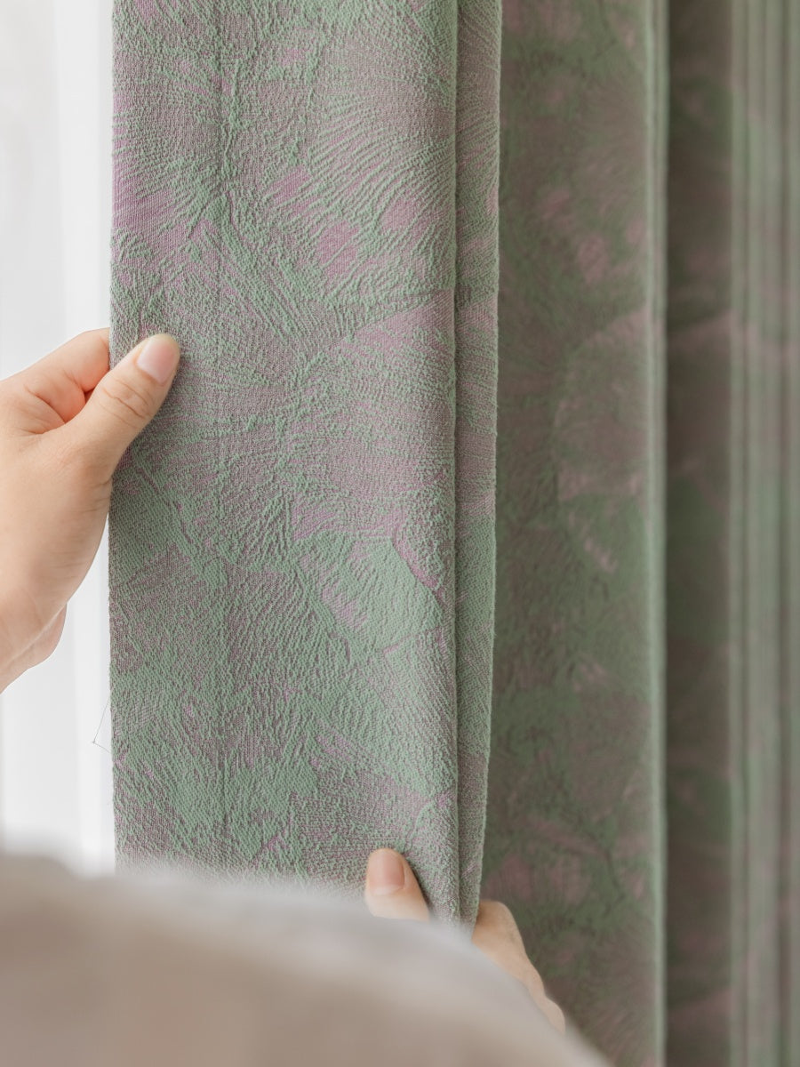Close-up of a hand holding green jacquard curtain with ginkgo leaf pattern and textured fabric.
