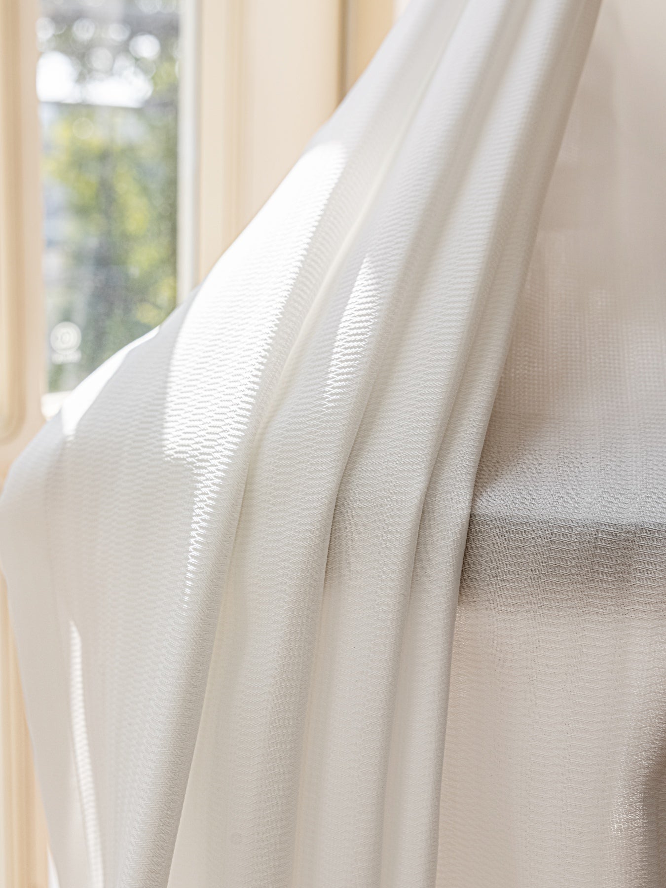 White sheer curtain hanging, providing light penetration and enhanced privacy with an elegant, soft white hue.