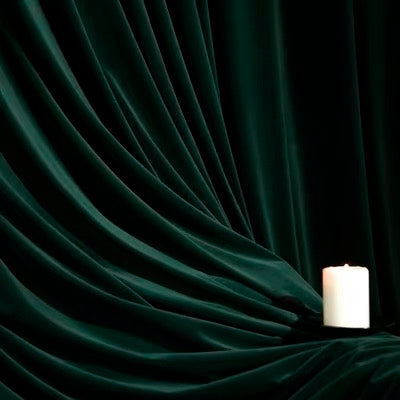 High-matte velvet drapes in deep green with a smooth, luxurious texture and elegant folds beside a white candle