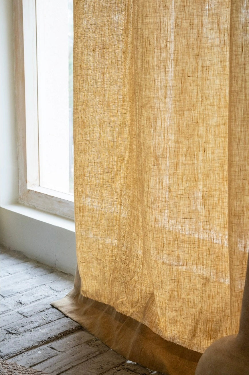 Mustard yellow curtains made from 100% French linen with a soft, muted yellow tone and natural texture hanging by a window.