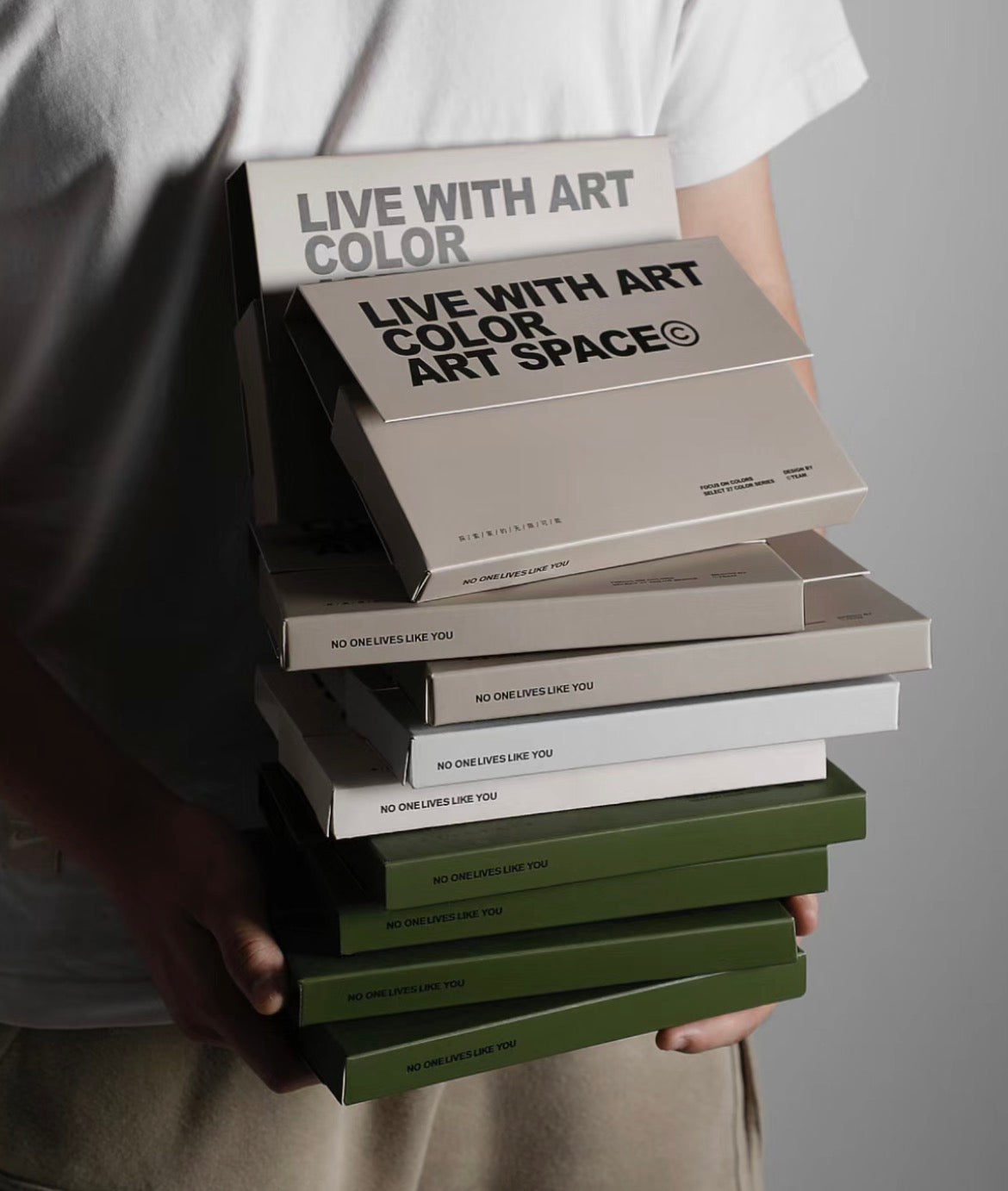 A person holding a stack of boxed fabric swatches in varying shades.