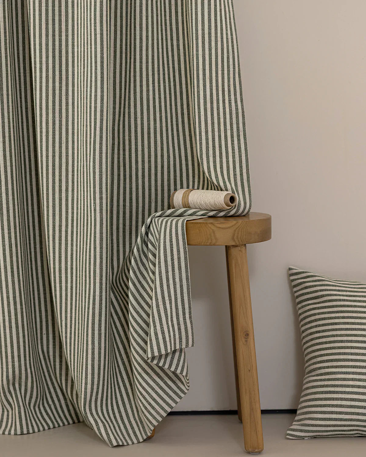 Classic linen striped curtains in neutral tones draped beside a wooden stool with matching striped cushion nearby