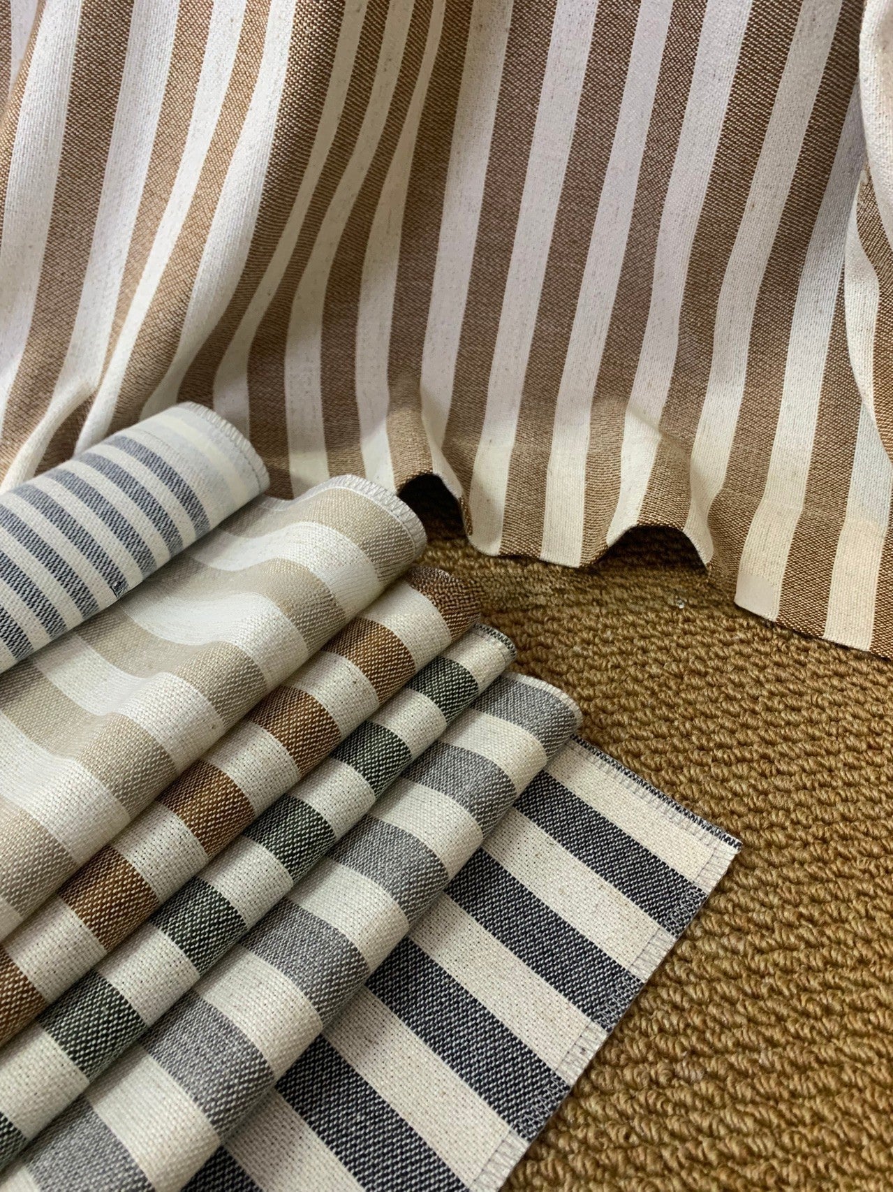 Close-up of classic linen striped curtains fabric samples in neutral tones with varying stripe widths on woven surface