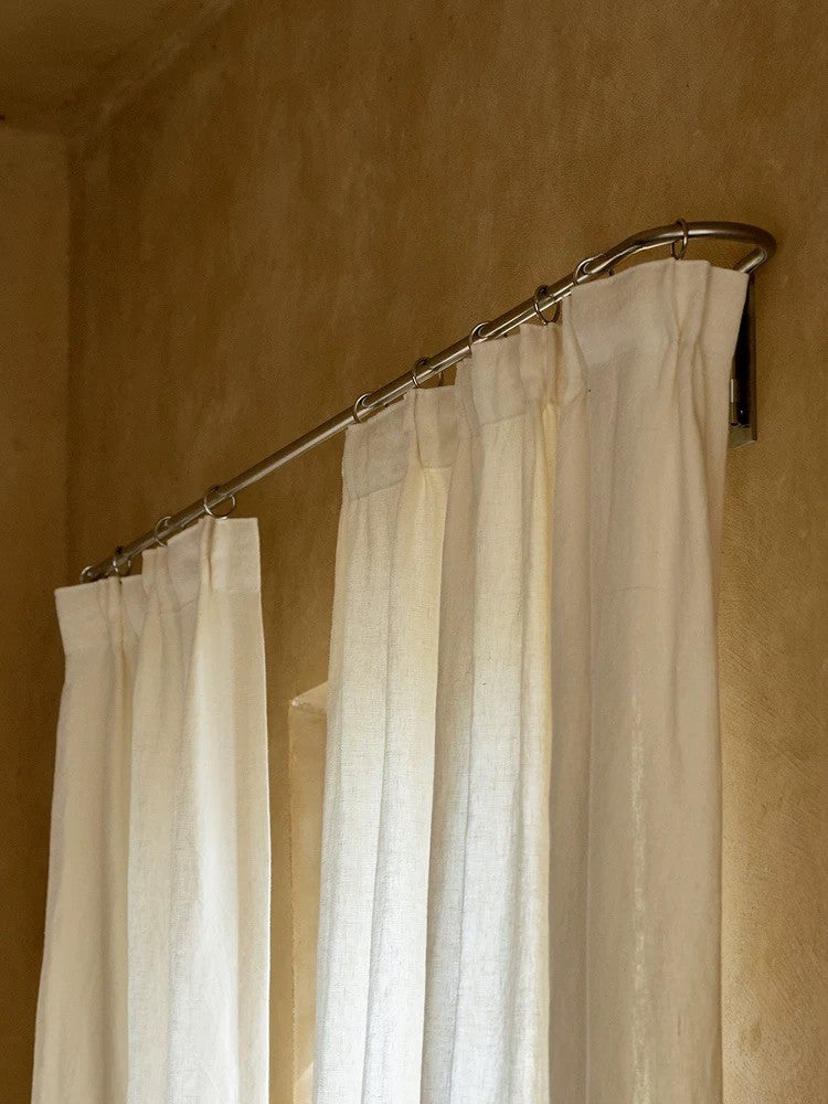 Ivory white linen curtains hanging on metal rod in warm-toned room interior