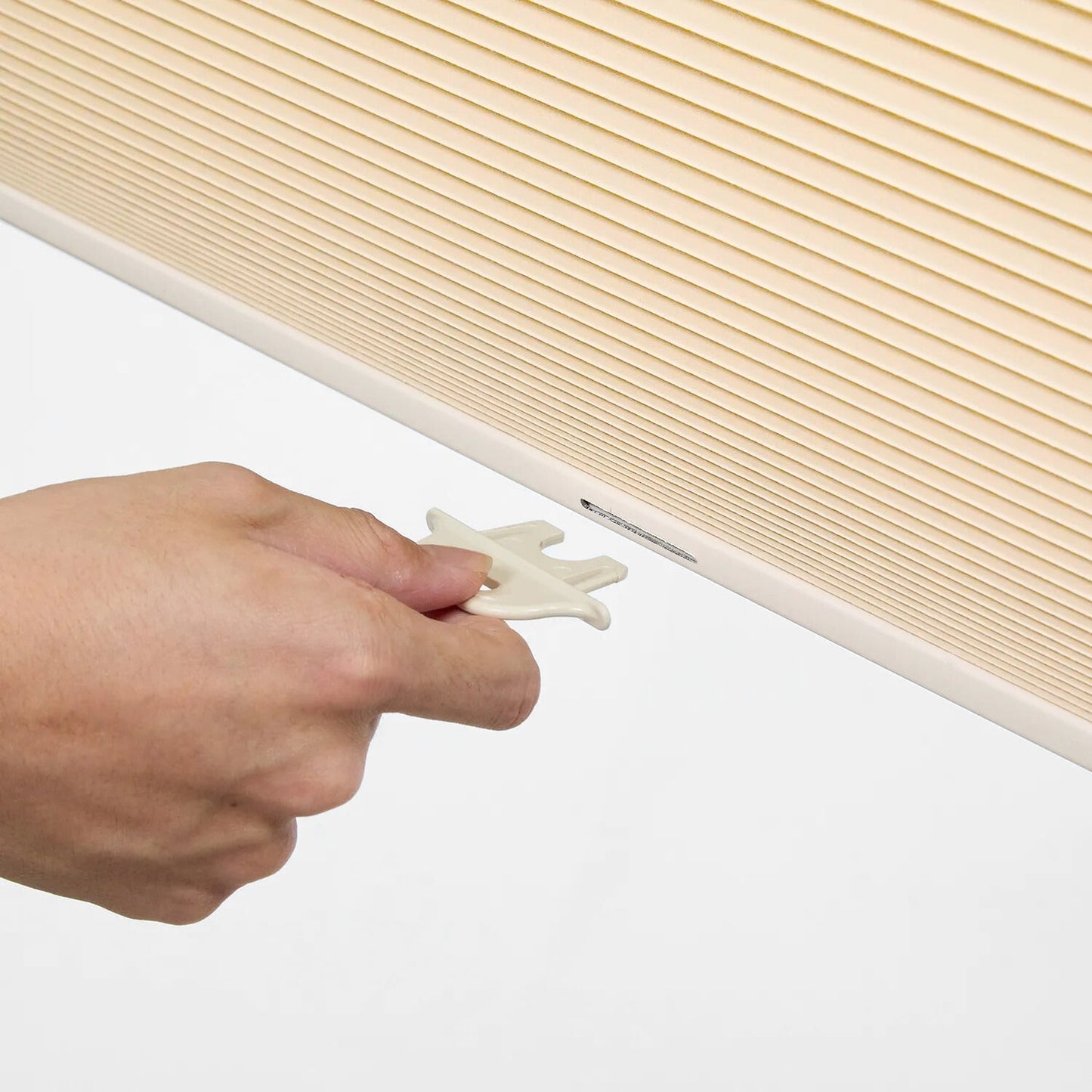 Hand installing beige no-drill honeycomb shades with tool-free silicone no-nail system on window frame