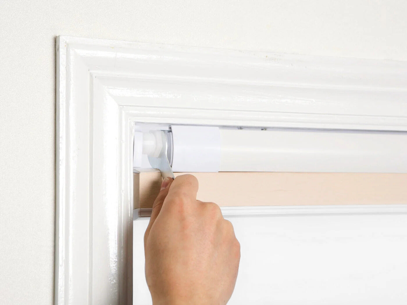 Hand installing no-drill honeycomb shades with silicone no-nail system on a white window frame