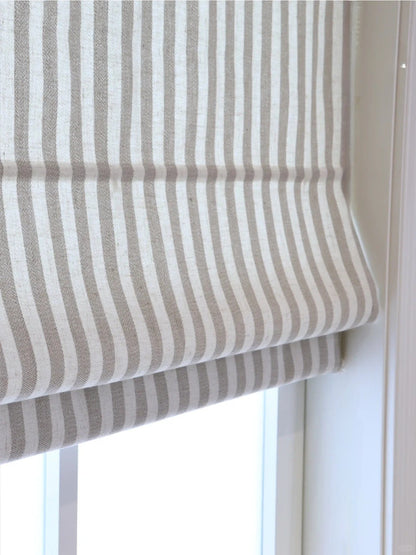 Close-up of beige and white striped Roman shades with cordless lift system covering a window