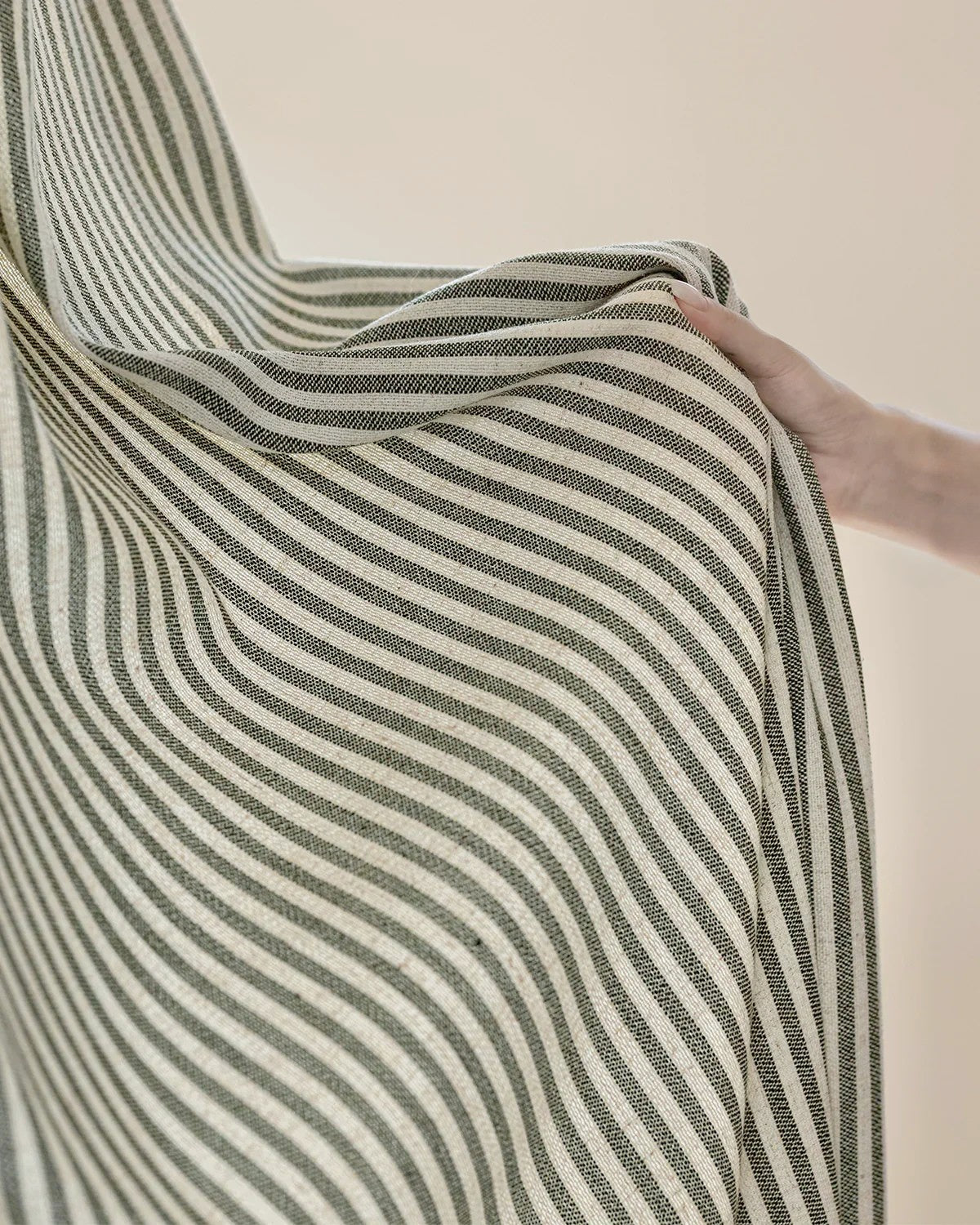 Hand holding classic linen striped curtains with fine neutral stripes, showing fabric texture and drape