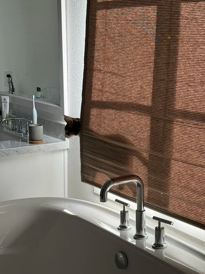 bathroom with bamboo roman shades partially filtering sunlight over a modern bathtub and sink area
