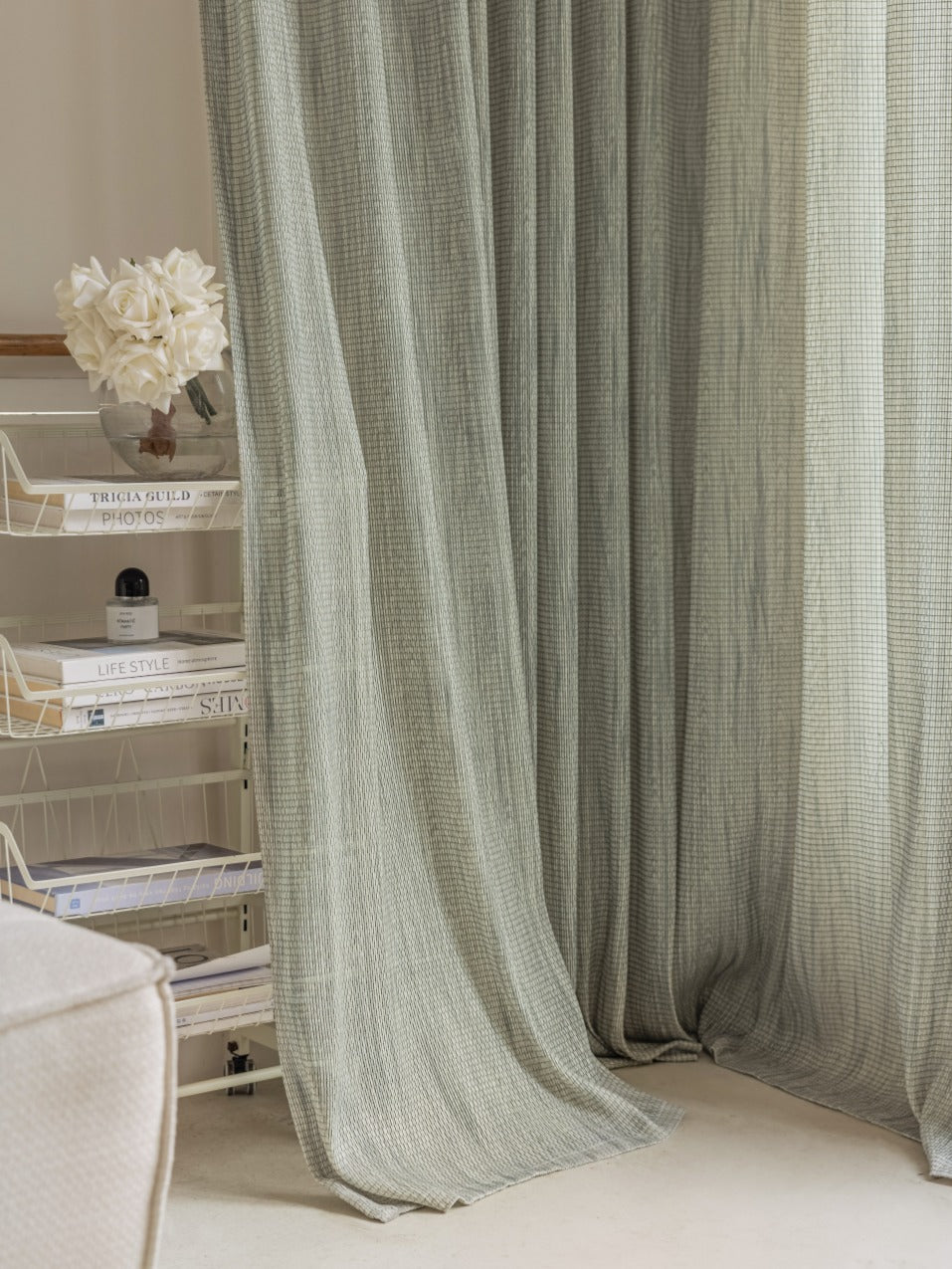 Smoky green sheer curtain with mesh grid design imported from Germany, displayed in a sophisticated living room setting with magazine rack in the background