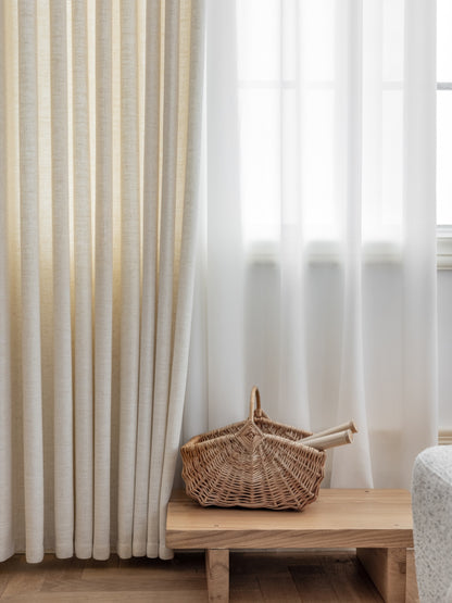 Luxury white French linen blend pleated drapes in a beautifully lit room with a wooden bench and woven basket, perfect for upscale modern interiors
