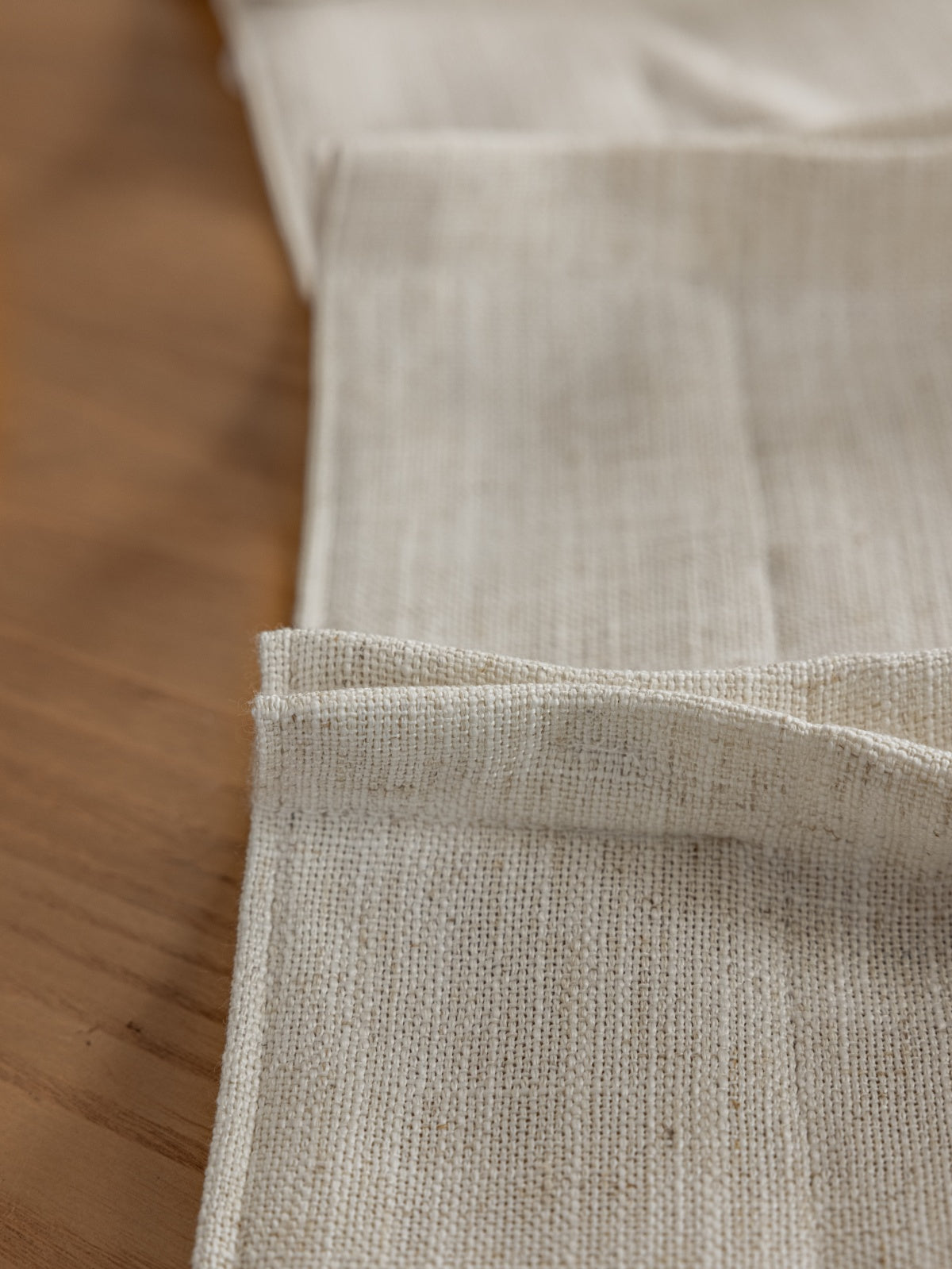 Close-up of white French linen blend drape with fine texture and precise hemming on a wooden surface, illustrating luxury and quality
