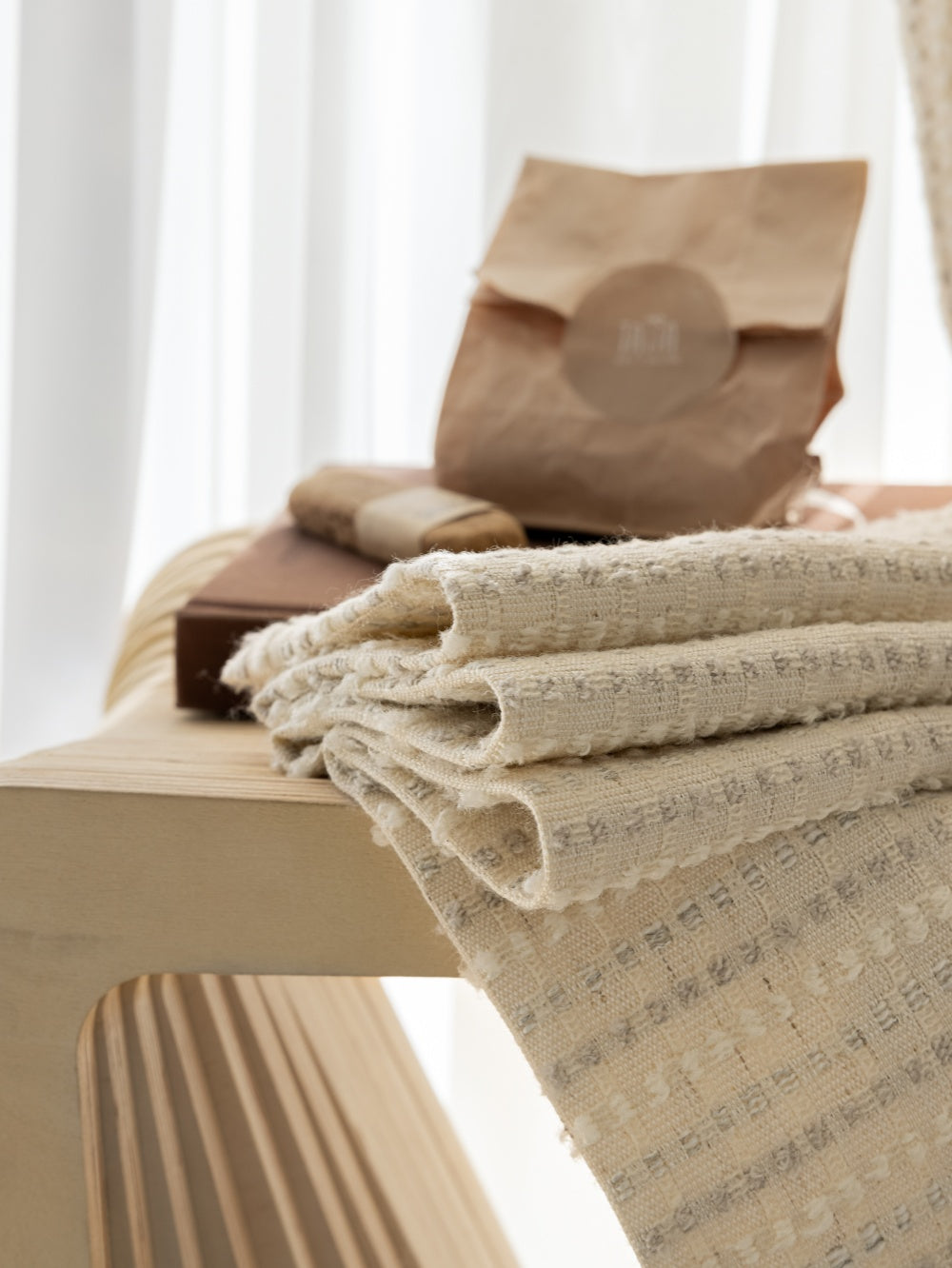 Designer white blackout curtains with subtle stripes inspired by Agnes Martin, folded on a beige table.