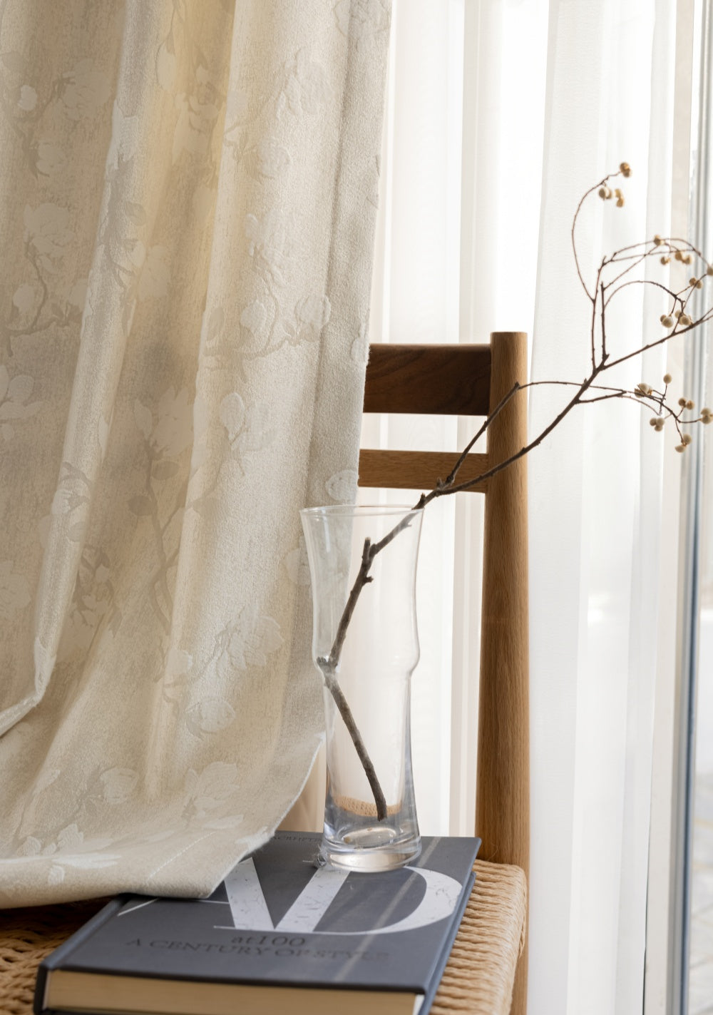 Luxury magnolia embroidery pattern curtains in cream color, draped over a chair with a vase and books nearby.