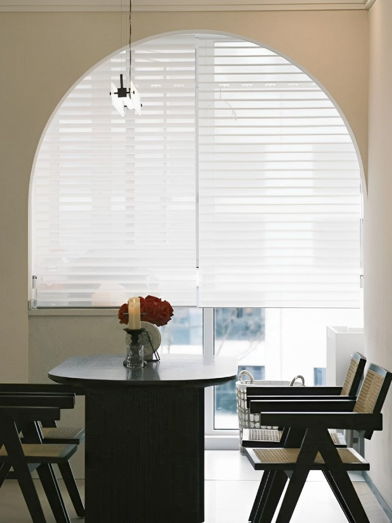 Light-filtering sheer shades on arched window in modern dining area.