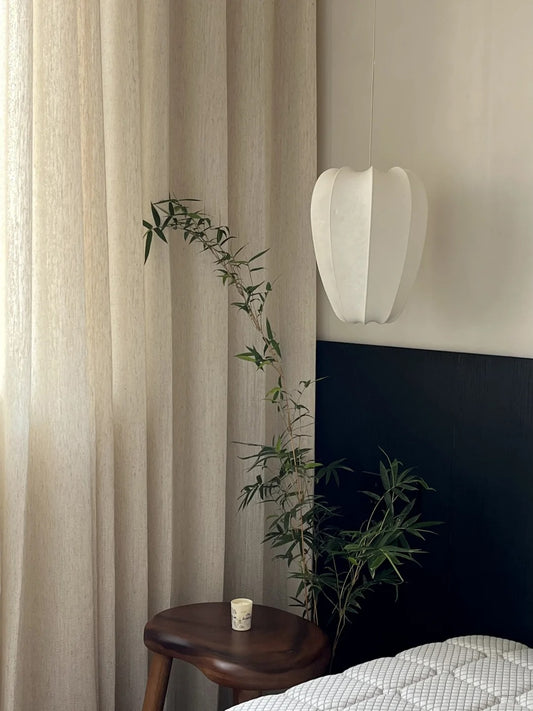 Sheer linen-wool blend curtain in oatmeal color enhancing privacy while allowing natural light in a stylishly decorated room with wooden stool and greenery