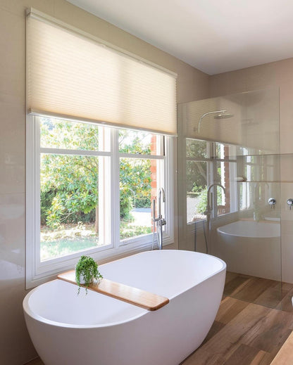 Luxurious bathroom interior with top-down bottom-up honeycomb shades on window, standalone bathtub, wooden floor, and glass shower, demonstrating elegant window treatment solutions.