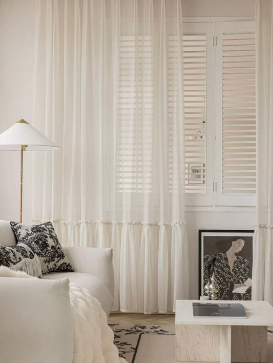 Elegant sheer curtains in a soft apricot hue framing a window, accompanied by plush white sofa with patterned cushions in a serene living room setting