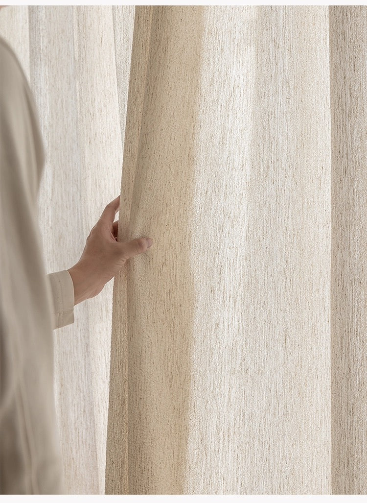 Close-up of a person's hand pulling aside a linen-wool blend sheer curtain in a natural oatmeal hue, casting a gentle light and enhancing home decor