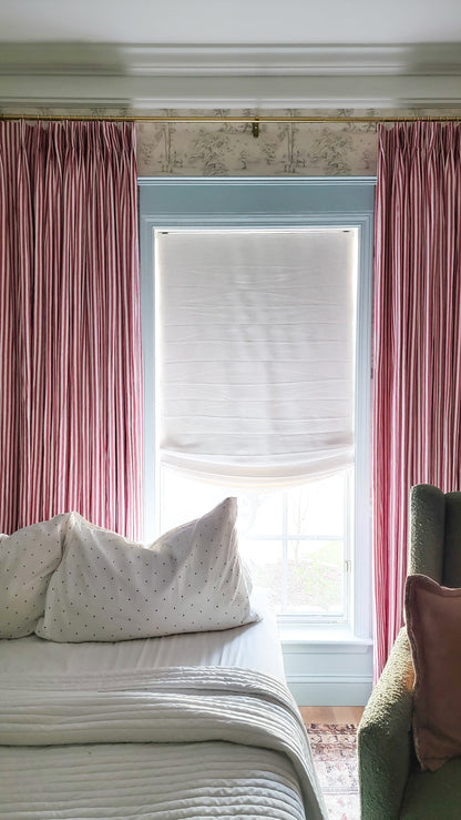 Soft Curve Relaxed Roman Shades in white linen with cordless lift, fitted on window with red drapes in cozy bedroom