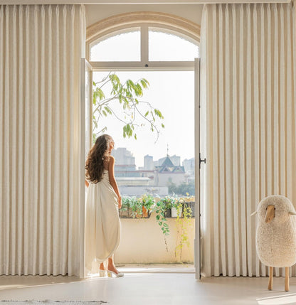 Elegant white blackout curtains with French embossed design in a bright living room with large window and a woman standing near the doorway