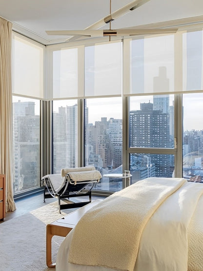 A cozy bedroom with a curtain-draped large window, offering a breathtaking view of the cityscape beyond.