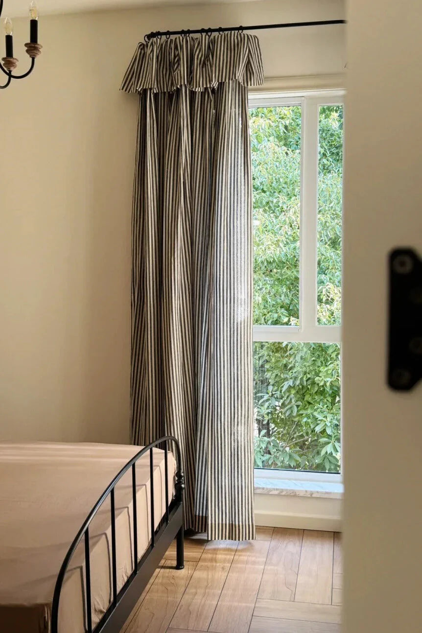 Classic linen striped curtains with fine vertical stripes in neutral tones hanging in bedroom window with black metal bedframe and wooden floor
