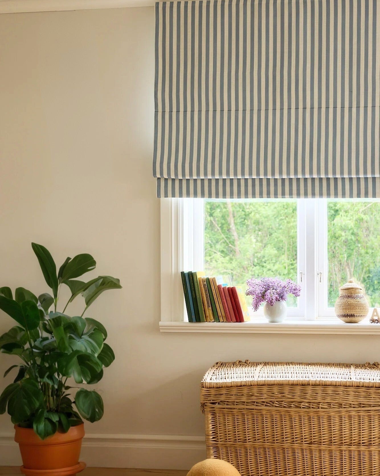 Striped Roman shades with cordless lift, light filtering fabric, and classic blue and white stripes over window with plants and wicker basket