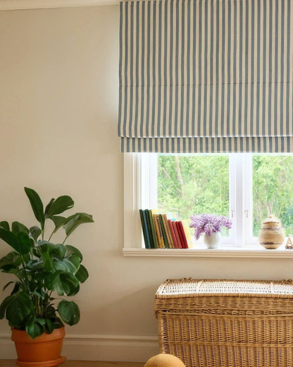 Striped Roman shades with cordless lift, light filtering fabric, and classic blue and white stripes over window with plants and wicker basket
