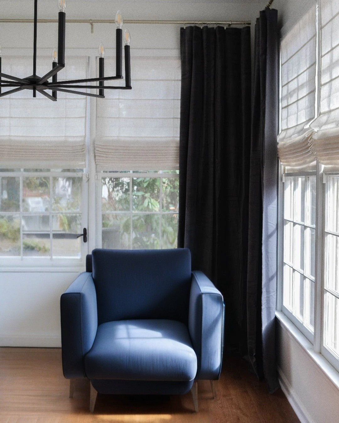Modern living room with cordless custom roman shades in light-filtering fabric and dark blackout curtains beside a blue armchair and large windows