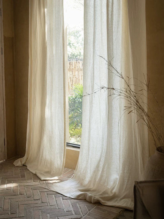 Sheer white linen curtains softly draping a sunlit window in a cozy living room setting