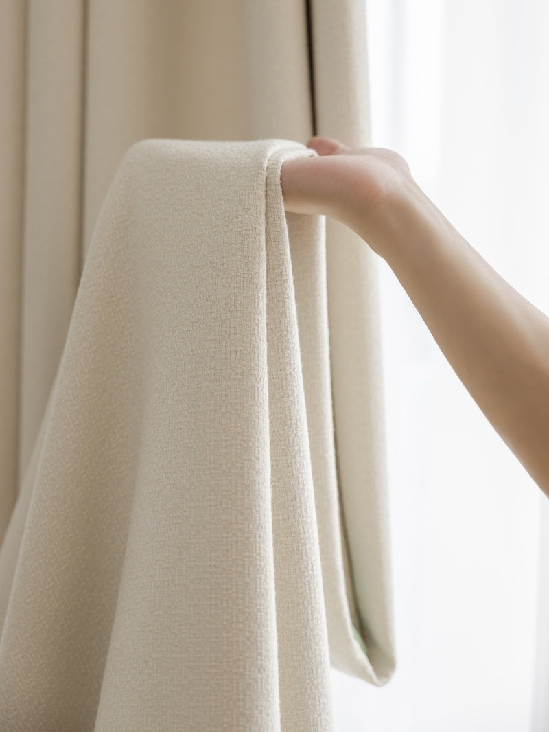 Close-up view of a hand holding a cream-colored heavyweight linen blend curtain, demonstrating the fabric's texture and elegance