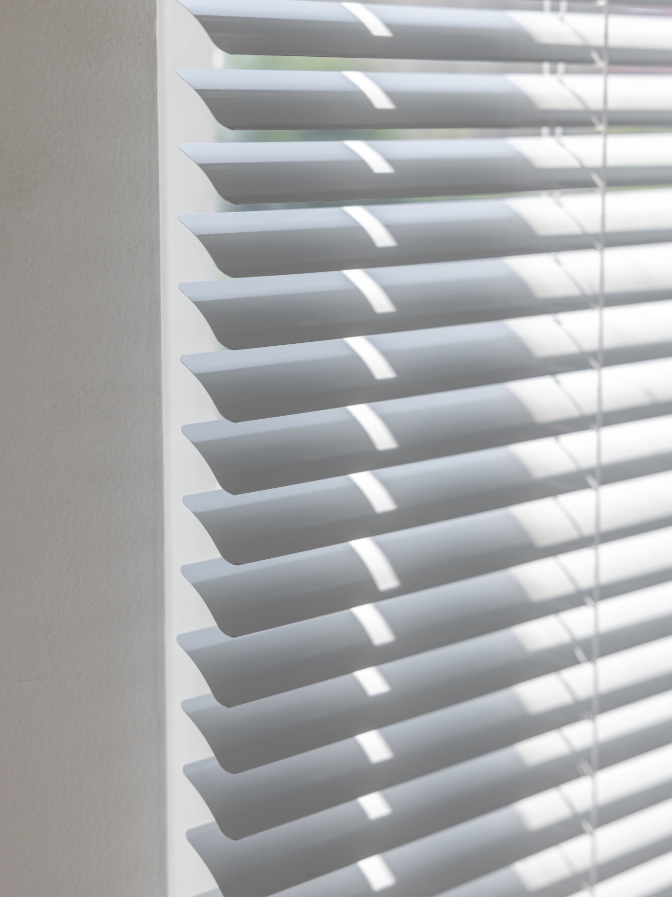 White vinyl mini blinds partially opened, casting soft shadows on a wall, showcasing simplistic design and functionality