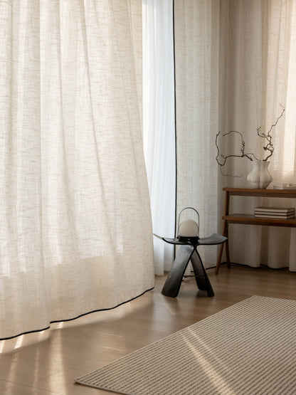 High-quality neutral linen drapes in a stylish living room with natural light, complemented by a minimalist stool, decorative branch, and textured rug