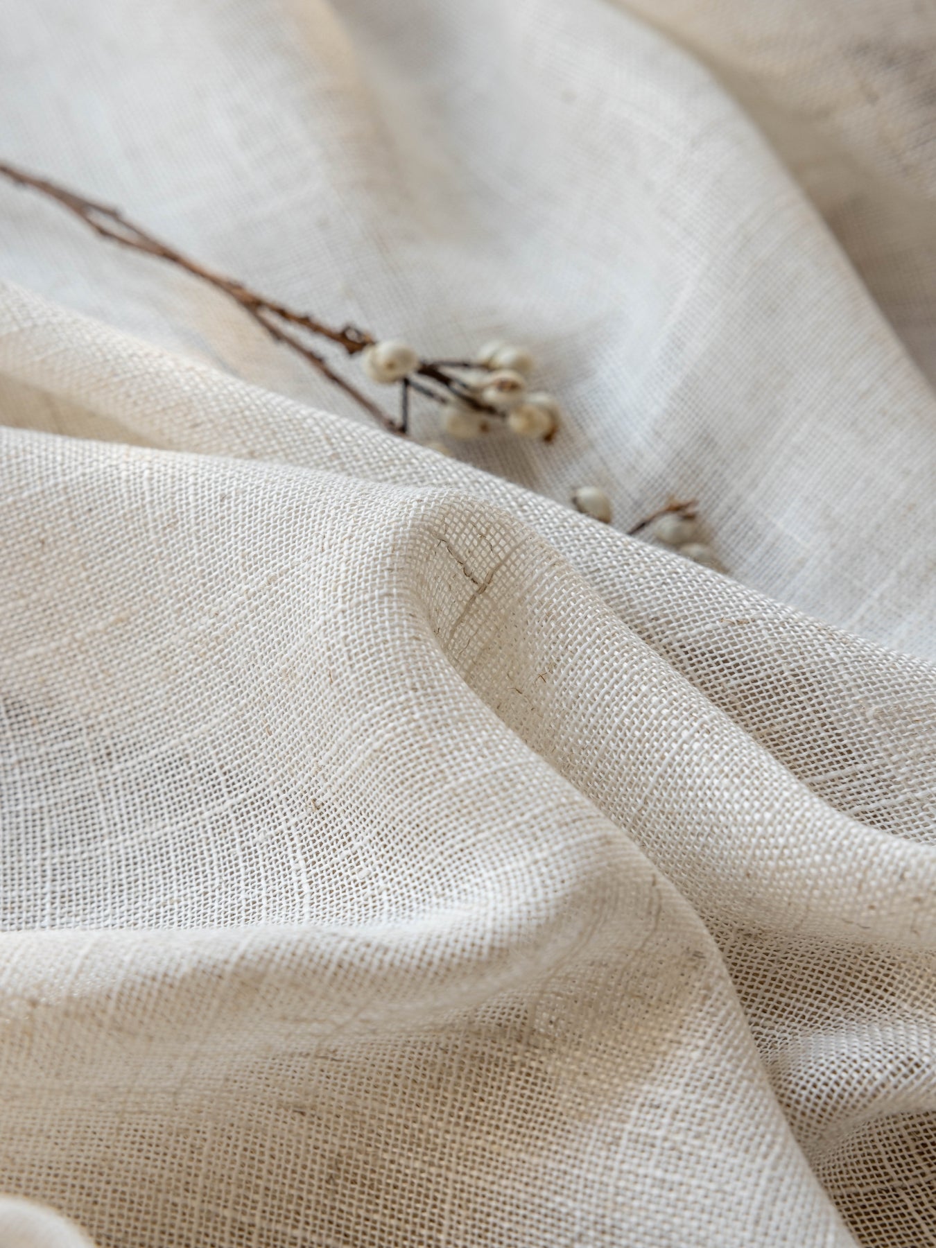 Close-up of luxurious linen drape with natural textured weave and dried botanical twigs accentuating its eco-friendly material