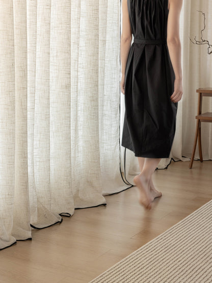 Elegant black-trimmed linen curtains in a sophisticated living room setting, with a stylishly dressed woman subtly enhancing the luxurious ambiance