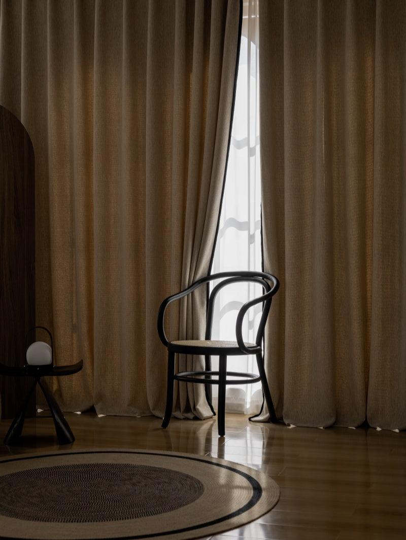 A chair positioned in front of a window, accompanied by premium drapery for bedroom, ensuring excellent shading in a dark room.