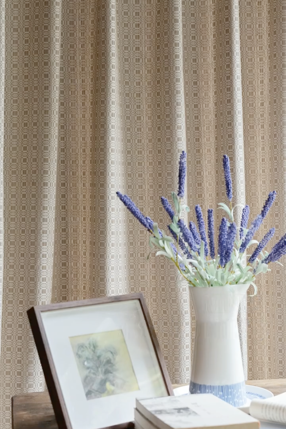 Beige vintage curtains with geometric pattern, styled with a vase of lavender flowers and framed artwork on a wooden table.