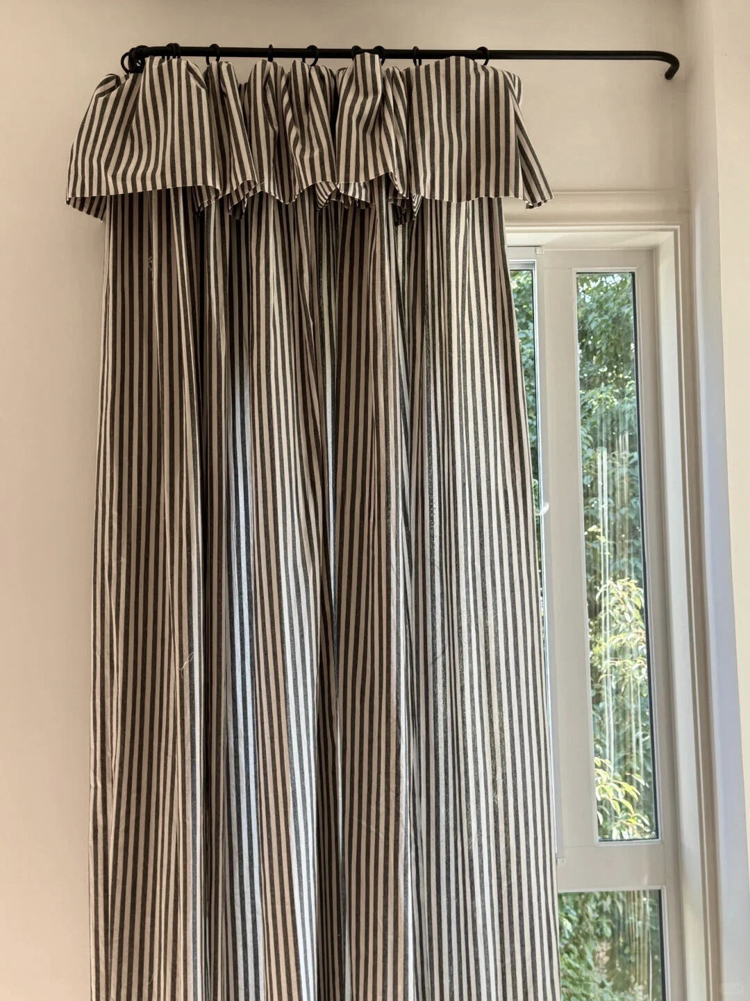 Striped curtains in neutral tones with fine vertical stripes hanging on a black rod by a window with natural light