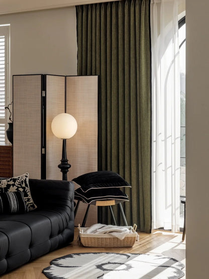 Luxurious heavyweight chenille green curtain draped in a stylishly furnished bedroom, complementing a black leather couch and modern decor elements