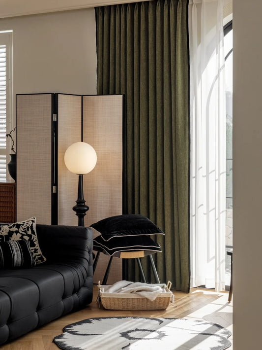 Luxurious heavyweight chenille green curtain draped in a stylishly furnished bedroom, complementing a black leather couch and modern decor elements