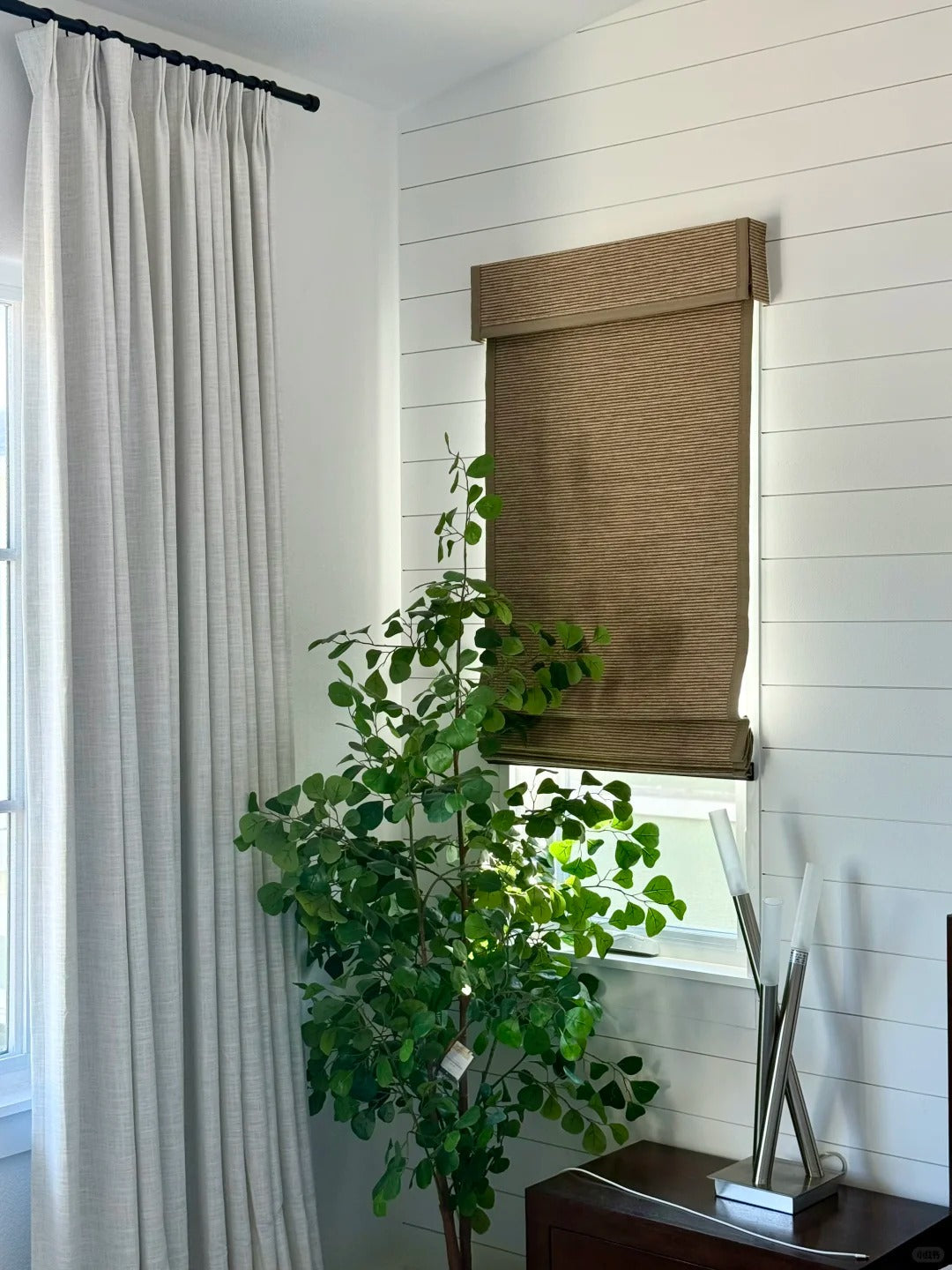 brown bamboo roman shade with soft light filtering in modern white room with plant and curtains
