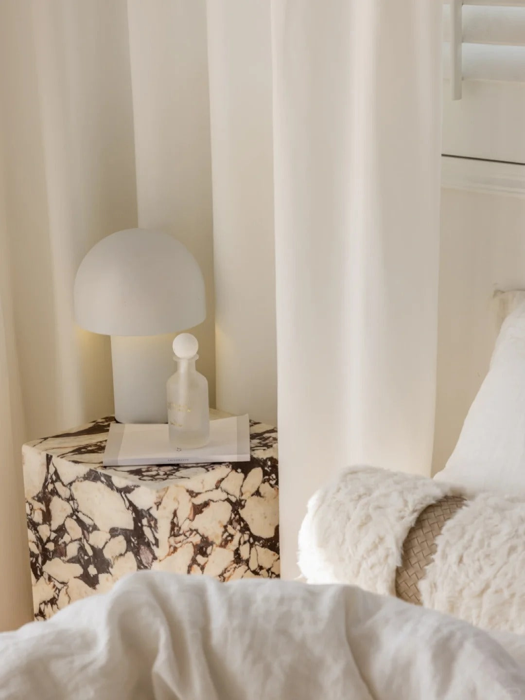 Elegant bedroom with white sheer curtain providing privacy, marble nightstand with modern lamp and cozy white blanket, emphasizing light penetration and room elegance