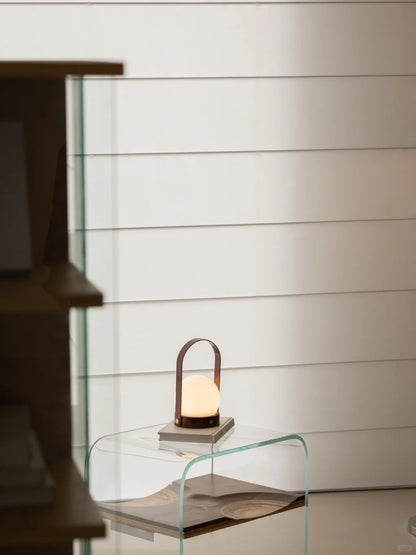 Modern portable lamp on a glass side table against a simple white wall, enhancing a contemporary interior decor