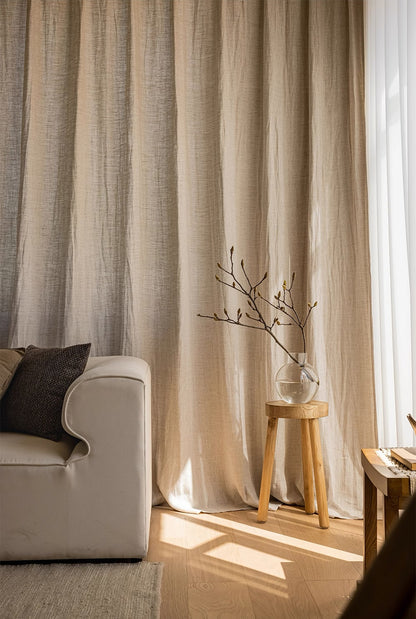 Elegant natural linen curtains cascading beside a modern sofa and wooden stool with minimalistic twig decor, exemplifying sophisticated home decor